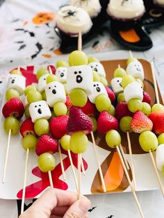 someone is holding up some fruit skewers with bears on them and other food items in the background