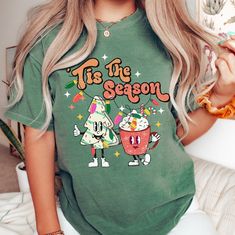 This Tis the Season Christmas shirt is a Comfort Colors retro Christmas t-shirt.  This cute Christmas tee is made of a soft-washed, garment-dyed fabric that brings extra coziness to your wardrobe. The relaxed fit makes it an excellent daily choice. If you want an oversized look, go up 1 to 2 sizes. The double-needle stitching throughout the tee makes it highly durable while the lack of side-seams helps the shirt retain its tubular shape. The shirt is dyed after it's been constructed, giving it a soft color and texture. 🏝 100% ring-spun cotton 🏝 Relaxed fit - If you want an oversized look, order 1 to 2 sizes larger than normal. If you want it to fit more like a micro mini t-shirt dress, order at least 2 sizes up. Care Instructions: Machine wash: cold (max 30C or 90F); Do not bleach; Tumbl Green Christmas Crew Neck T-shirt, Green Cotton Christmas Tops, Green Cotton Holiday Top, Christmas Green Cotton Tops, Green Cotton Top For Holidays, Casual Green Christmas Shirt, Green Graphic Print T-shirt For Winter, Winter Green Graphic Print T-shirt, Christmas Green Cotton T-shirt