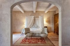 an archway leading to a bedroom with a white bed and chair in it, along with a rug on the floor