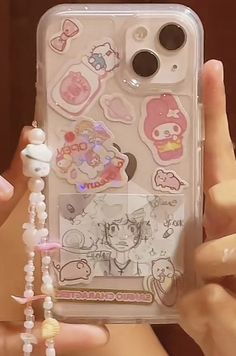 someone is holding up their phone case with stickers on it and beads hanging from the back