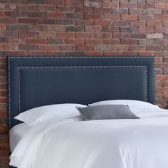 an upholstered headboard on a bed in front of a red brick wall