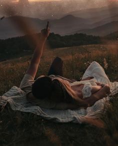 a person laying on top of a blanket in the grass with their hand raised up