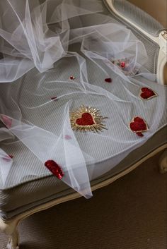 a white bed with red hearts on it's cover and some veils around the headboard