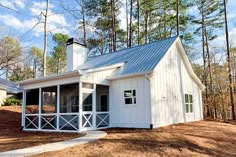 a small white house in the woods with a metal roof and windows on it's side