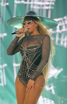 a woman in a bodysuit and hat on stage with a microphone to her side