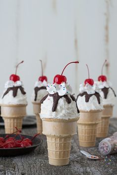 ice cream sundaes with cherries and whipped cream in cones on a table