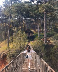 a woman walking across a wooden bridge in the woods