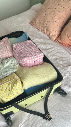 an open suitcase sitting on top of a bed filled with pillows and blankets next to pillow cases