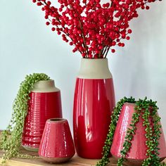 three red vases with flowers in them on a wooden shelf next to other items