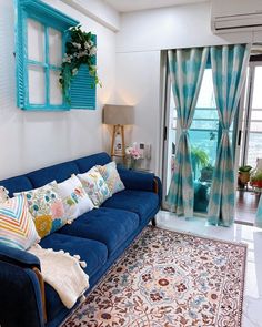 a blue couch sitting in front of a window next to a rug and table with flowers on it