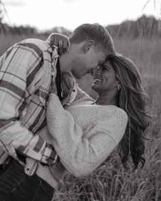 black and white photograph of a couple kissing in tall grass with trees in the background