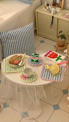 a table with plates and cups on it in a room next to a bed that has blue and white striped pillows