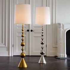 two lamps sitting next to each other on top of a wooden floor in front of a fireplace