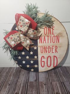 a wooden sign that says one nation under god with bows and evergreen branches on it