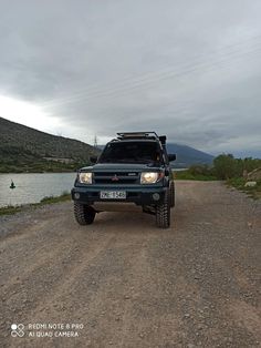 a truck parked on the side of a dirt road next to a body of water