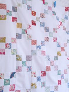 a quilt hanging on a clothes line in front of a wall with several different colored squares