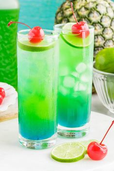 two glasses filled with blue and green liquid next to a pineapple on the side