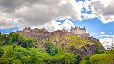 a castle on top of a hill surrounded by trees and bushes under a cloudy blue sky