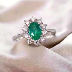 an emerald and diamond ring sitting on top of a white cloth