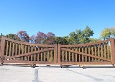 a large wooden gate in the middle of a parking lot next to trees and bushes