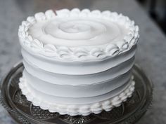 a close up of a white cake on a glass plate with frosting swirls