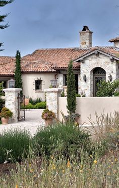 a large house with lots of plants in front of it and trees around the entrance