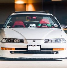 a white car parked in front of a building with its hood up and the lights on