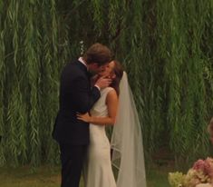 a bride and groom kissing in front of a willow tree at their outdoor wedding ceremony