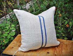 a pillow sitting on top of a wooden table in front of some bushes and trees