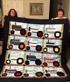 two women holding up a quilt made to look like tractors