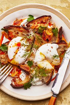 a white plate topped with fried eggs and vegetables next to a fork on top of a table