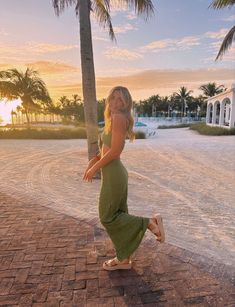 a woman in a green dress is dancing on the sidewalk near palm trees at sunset