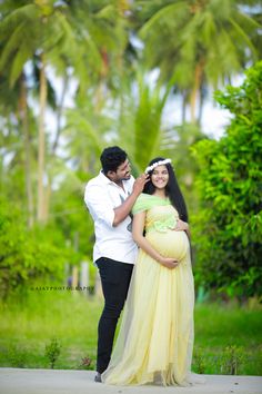 a pregnant couple standing in front of palm trees