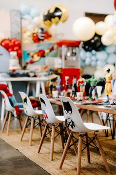 a room filled with lots of chairs and balloons in the air above it is a wooden table surrounded by white plastic chairs