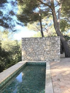 a stone wall next to a pool surrounded by trees and rocks on the side of a house