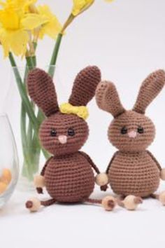 two crocheted rabbits sitting next to a vase filled with yellow flowers