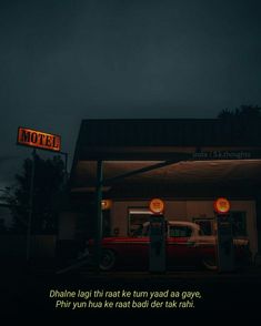 an old car is parked in front of a motel at night with the neon sign above it