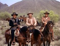 three men in cowboy hats are riding horses