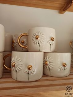 four white mugs with gold handles and daisies on them sitting on a shelf