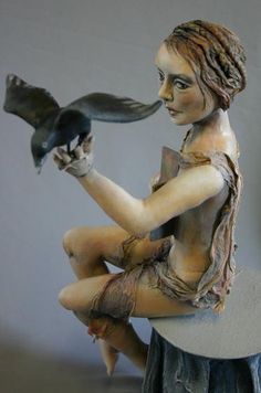 a statue of a woman sitting on top of a tree stump holding a bird in her hand