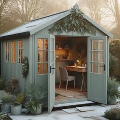 a garden shed with the door open and desk in it's center surrounded by potted plants