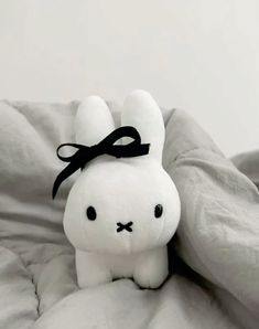 a white stuffed animal with a black bow on it's head sitting on a bed