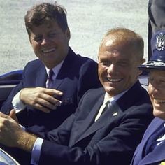 three men in suits and ties sitting next to each other on a car, smiling at the camera