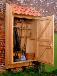 an open wooden storage shed with gardening tools in the door and on the outside wall