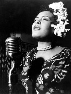 a black and white photo of a woman singing into a microphone with flowers in her hair