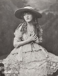 an old fashion photo of a woman in a dress and hat with her hands on her chest