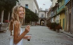 a woman standing in the middle of an alley way holding a drink and looking at the camera