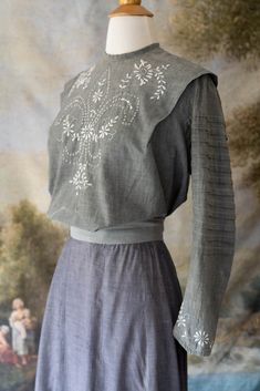 Incredibly beautiful and one of a kind 1900s Edwardian top and skirt set. This grey cotton set is beautifully accented with white embroidery on the front, sleeves, and bottom front of the skirt. The blouse is light dove grey with pleated layers to the narrow sleeves that end in embroidered wrists. The floral embroidery on the front of the blouse is intricate and oh so lovely. The waist is loose and is meant to be tied with the attached ribbons and then puffed up to give a pigeon front over the waist of the skirt. The blouse buttons down the back with white buttons and a hook and eye at the waist. The hem is unfinished, but will not be noticed when tucked in. The skirt is more a purple grey than the blouse. It has a narrow waist with a waistband that closes with a hook and eye and snaps in Victorian Cotton Fitted Blouse, Fitted Victorian Cotton Blouse, Long Sleeve Cotton Dress With Historical Design, Long Sleeve Cotton Dresses With Historical Design, Cotton Long Sleeve Dresses With Historical Design, Vintage Cotton Dress With Historical Design, Fitted Traditional Victorian Dress, Vintage Fitted Blouse With Intricate Embroidery, Fitted Vintage Blouse With Intricate Embroidery