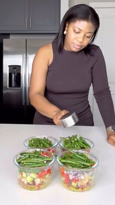 a woman in a kitchen preparing food on top of a white counter next to three bowls filled with green beans and other vegetables