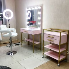 a pink vanity and stool in a room with mirrors on the wall, lights on